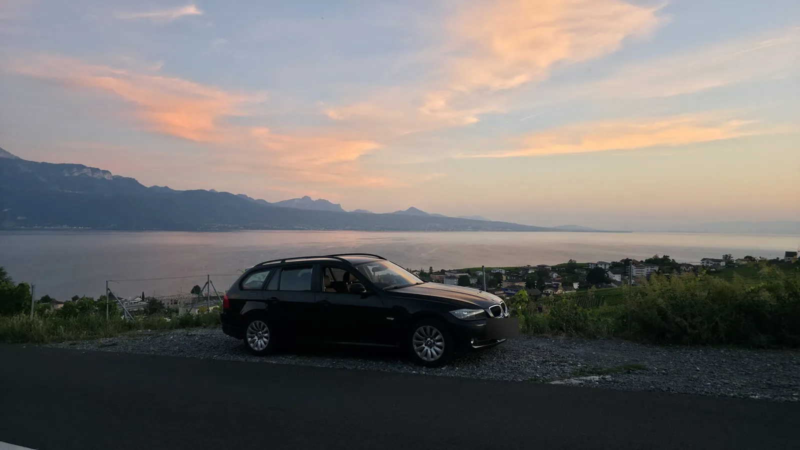 Break BMW Série 3 noir garé au-dessus du Léman au coucher du soleil, Alpes en arrière-plan